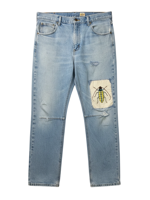 Lahad Vintage light-wash denim jeans with distressed details and a custom embroidered beetle patch on the right leg.